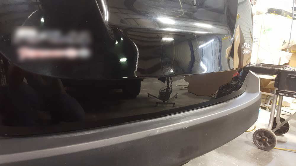 Rear view of a black vehicle showing a damaged bumper and tailgate inside a garage.