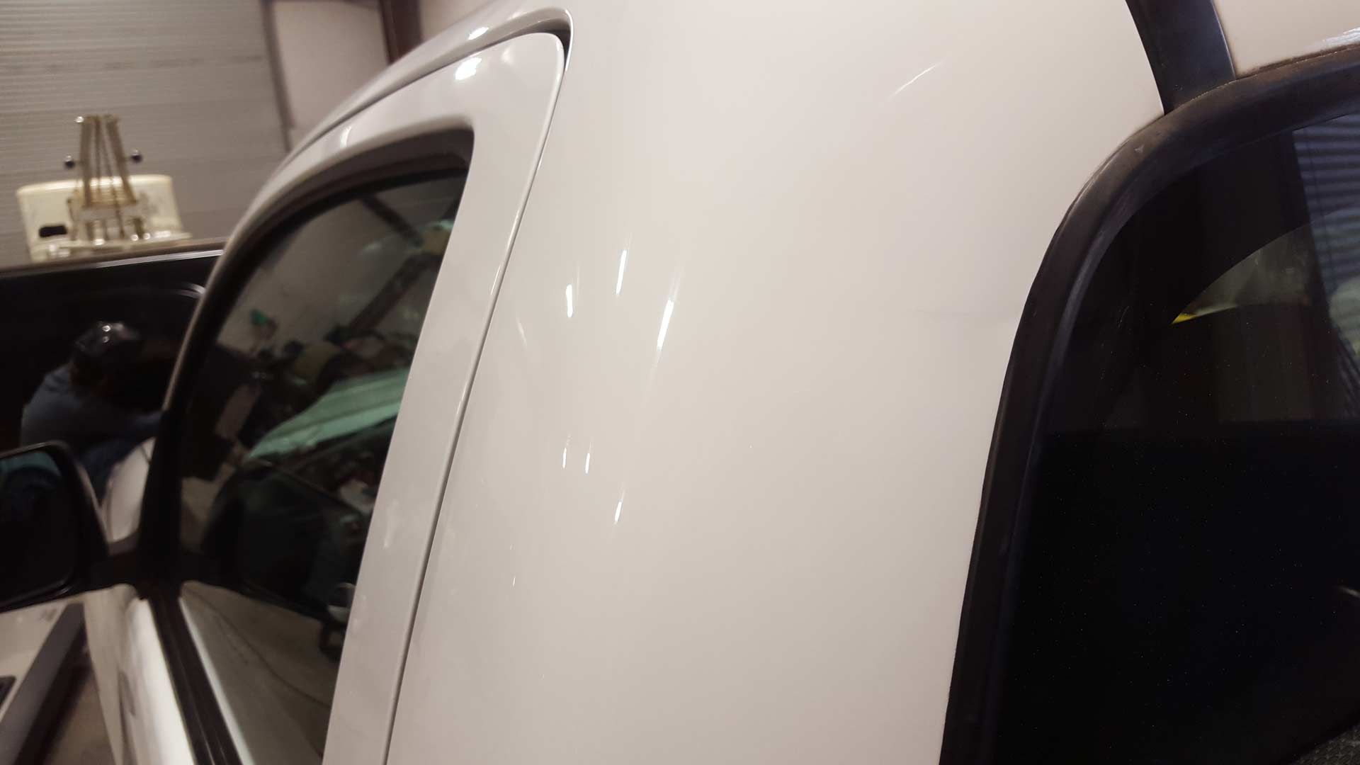Close-up of a white truck cab exterior, focusing on the B-pillar and door frame inside an auto shop.
