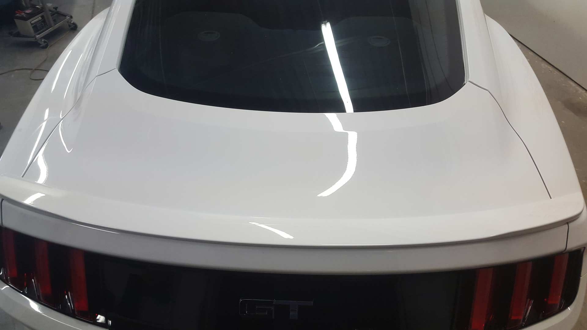 A close-up, high-angle shot of the rear trunk and spoiler of a white Ford Mustang parked in a garage.
