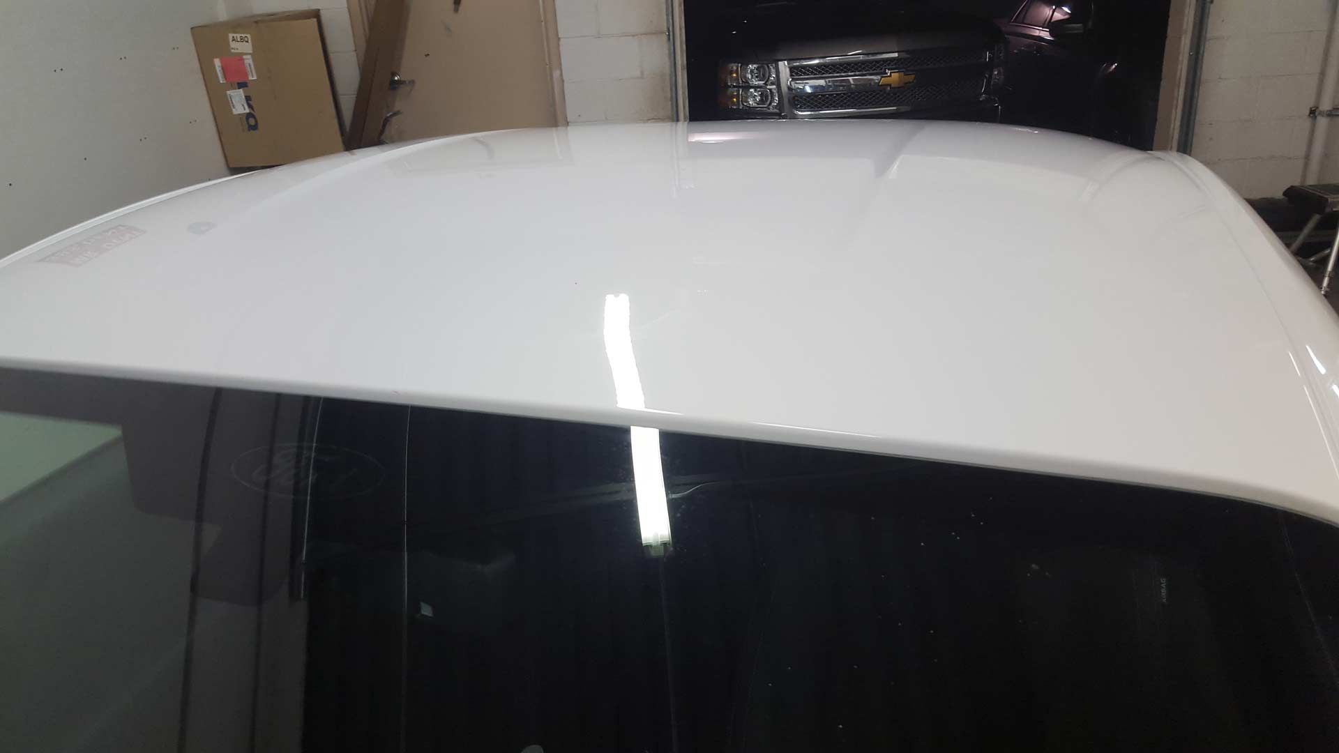 Close-up of a white truck cab exterior, focusing on the B-pillar and door frame inside an auto shop.