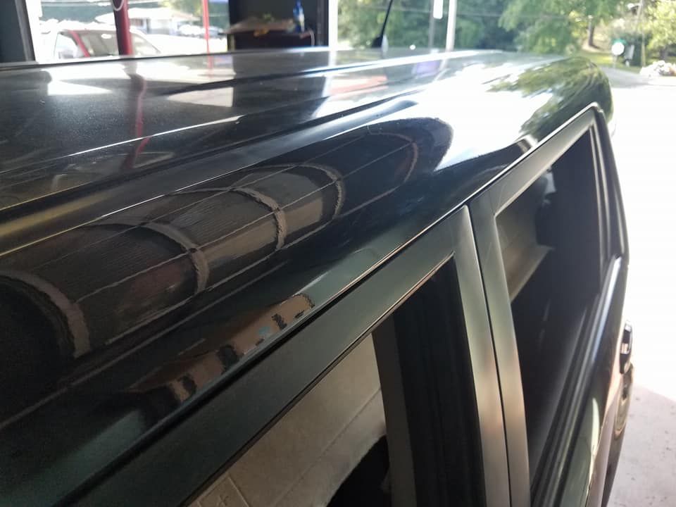A close-up, high-angle shot of a shiny, black vehicle roof and the top edge of the side window frame.