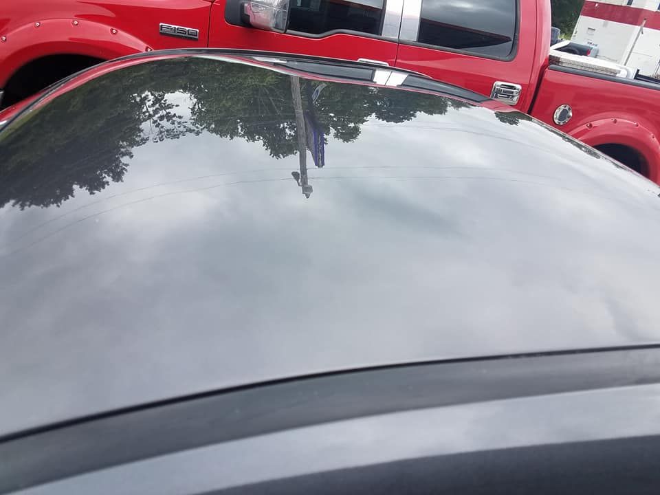 A dark gray car roof showing reflections, with a bright red truck parked in the background.