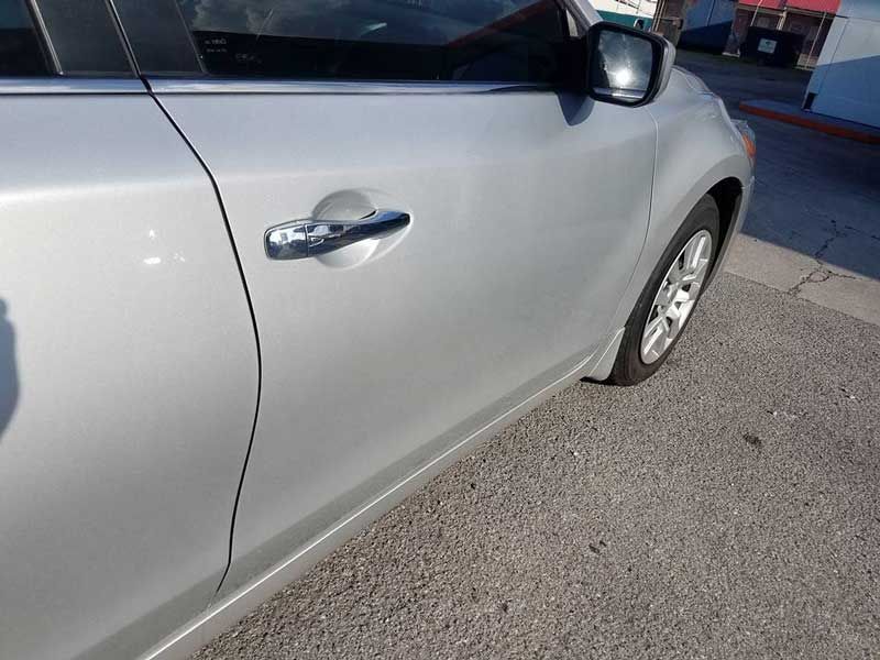A close-up, high-angle shot of a silver car's passenger-side door and front wheel, parked on asphalt.