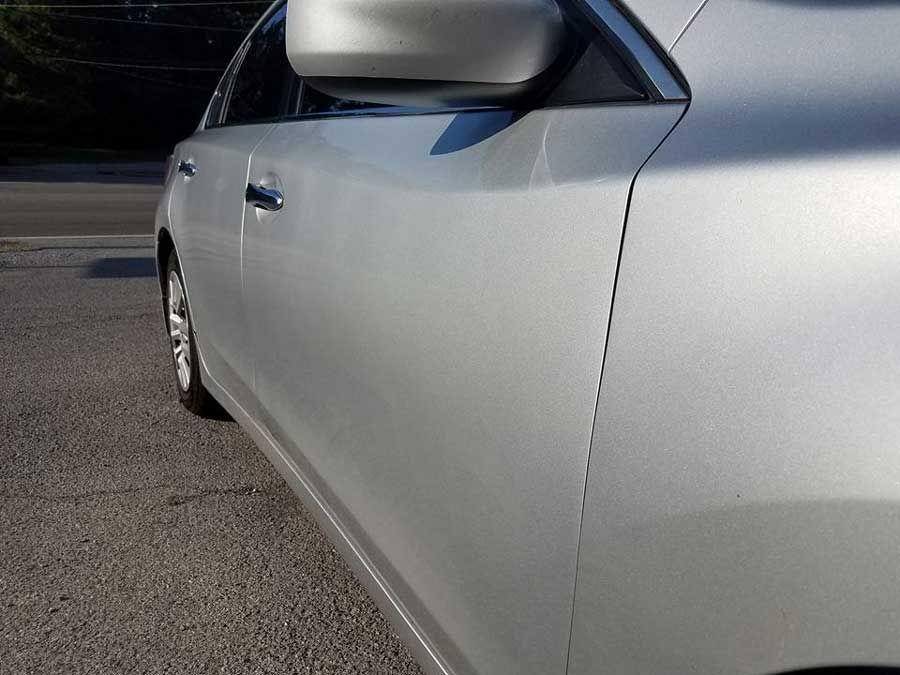 Side view of a silver sedan parked on asphalt, focusing on the front passenger door and side mirror.