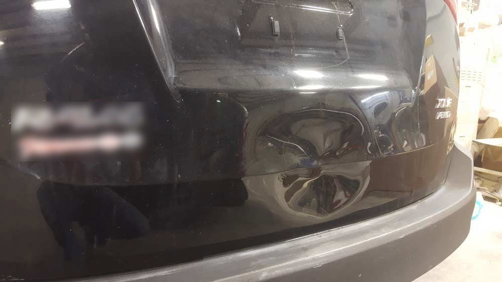 A dent in the center of a black vehicle's rear hatch door.