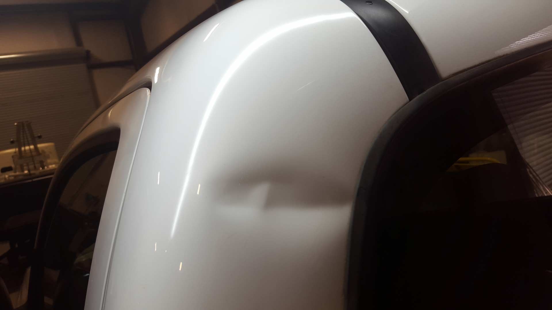 A close-up view of a noticeable dent on the white metal pillar of a vehicle near the rear window.