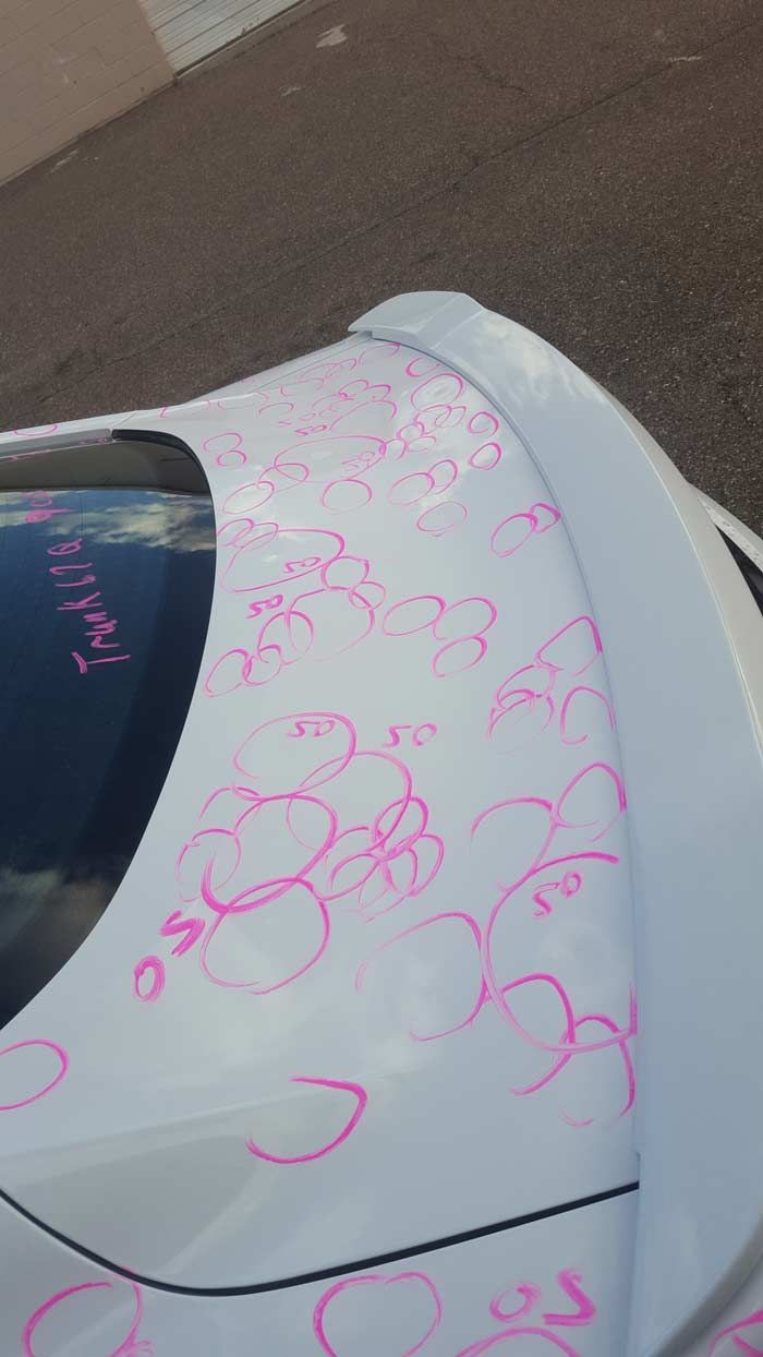 A white car trunk covered in pink hand-drawn circles and markings, possibly indicating areas for bodywork repair.