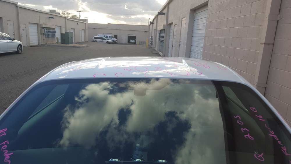 A close-up view of a noticeable dent on the white metal pillar of a vehicle near the rear window.