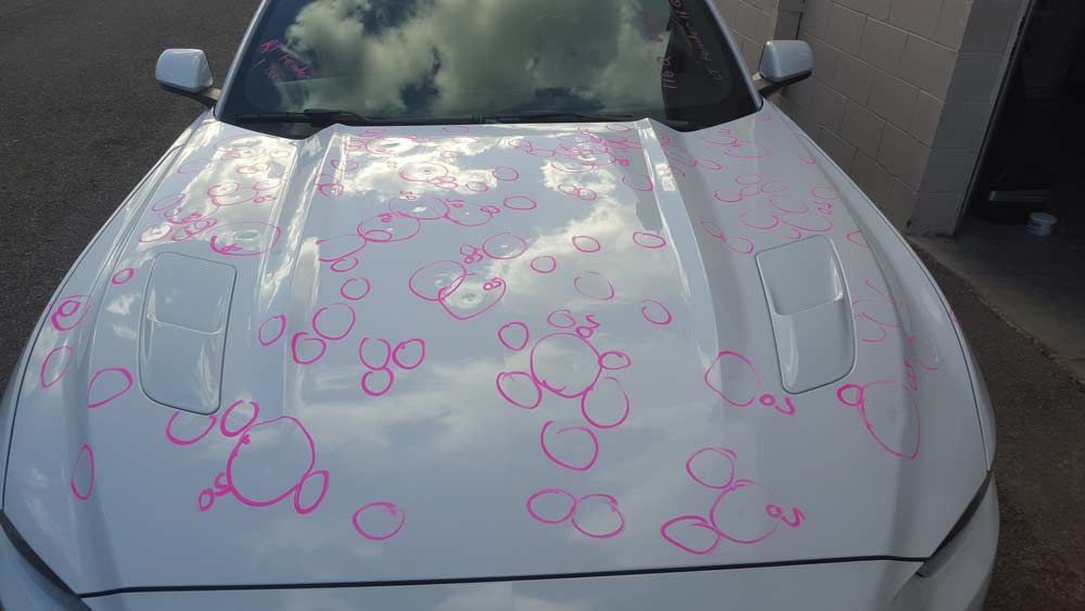White car hood with numerous circular indentations from hail damage, highlighted with pink marker circles.