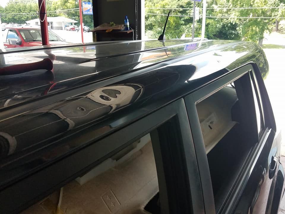 A close-up view of the roofline and window frame of a black vehicle in a garage, showing a tool resting on the roof.