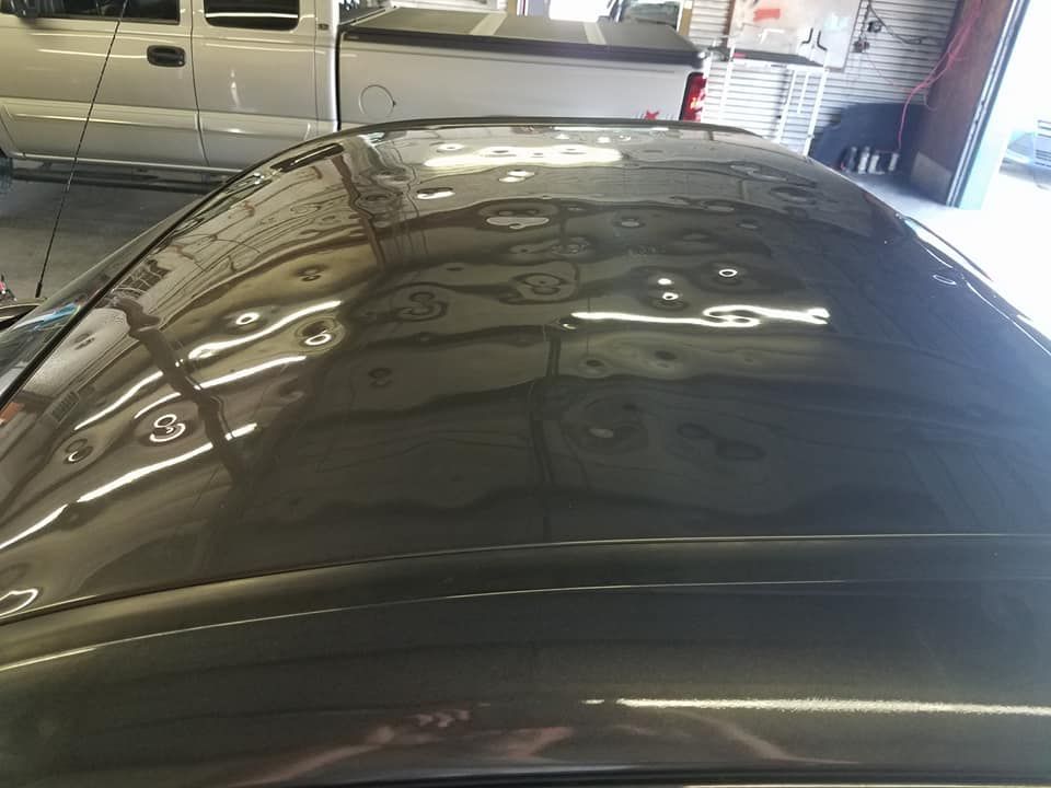 A dark-colored car roof covered in multiple small dents, likely from hail damage, parked inside a garage.
