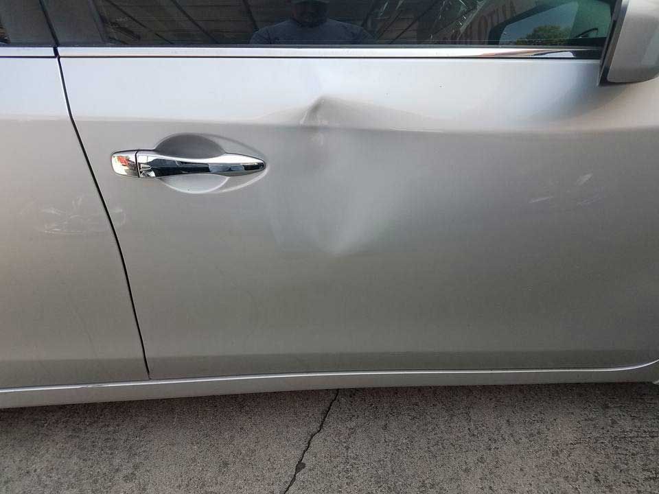 A silver car door with a noticeable dent located just above the door handle.