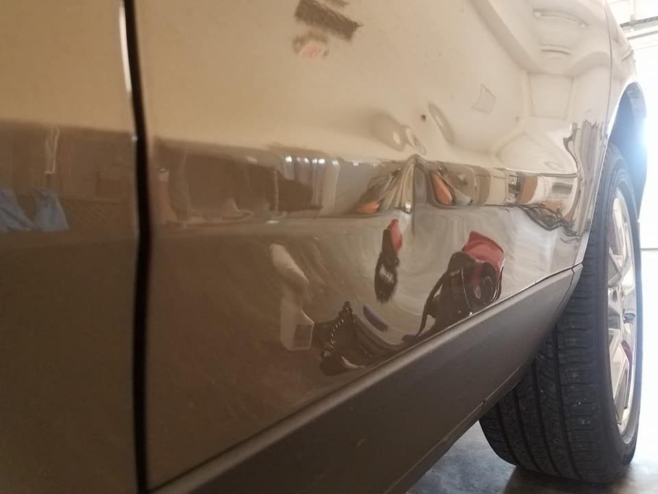 A side-view of a tan vehicle door showing a dented panel above the black rocker molding.