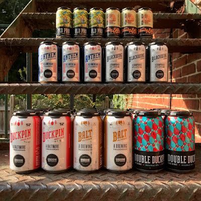 Assorted craft beer cans arranged on metal shelves outdoors, with colorful labels and brick steps behind them