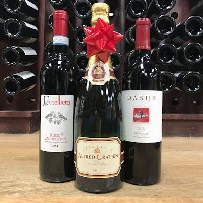 Three wine bottles on a shelf, with a central bottle topped by a red bow and star.