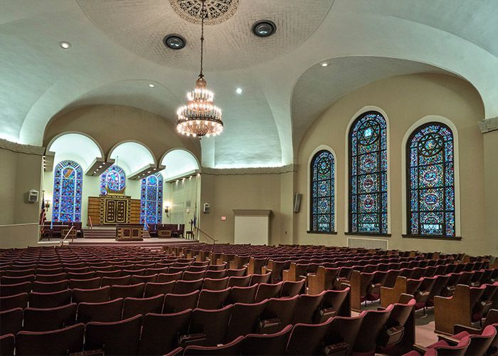 Interior of a synagogue with rows of seats, arched windows, and a central chandelier.