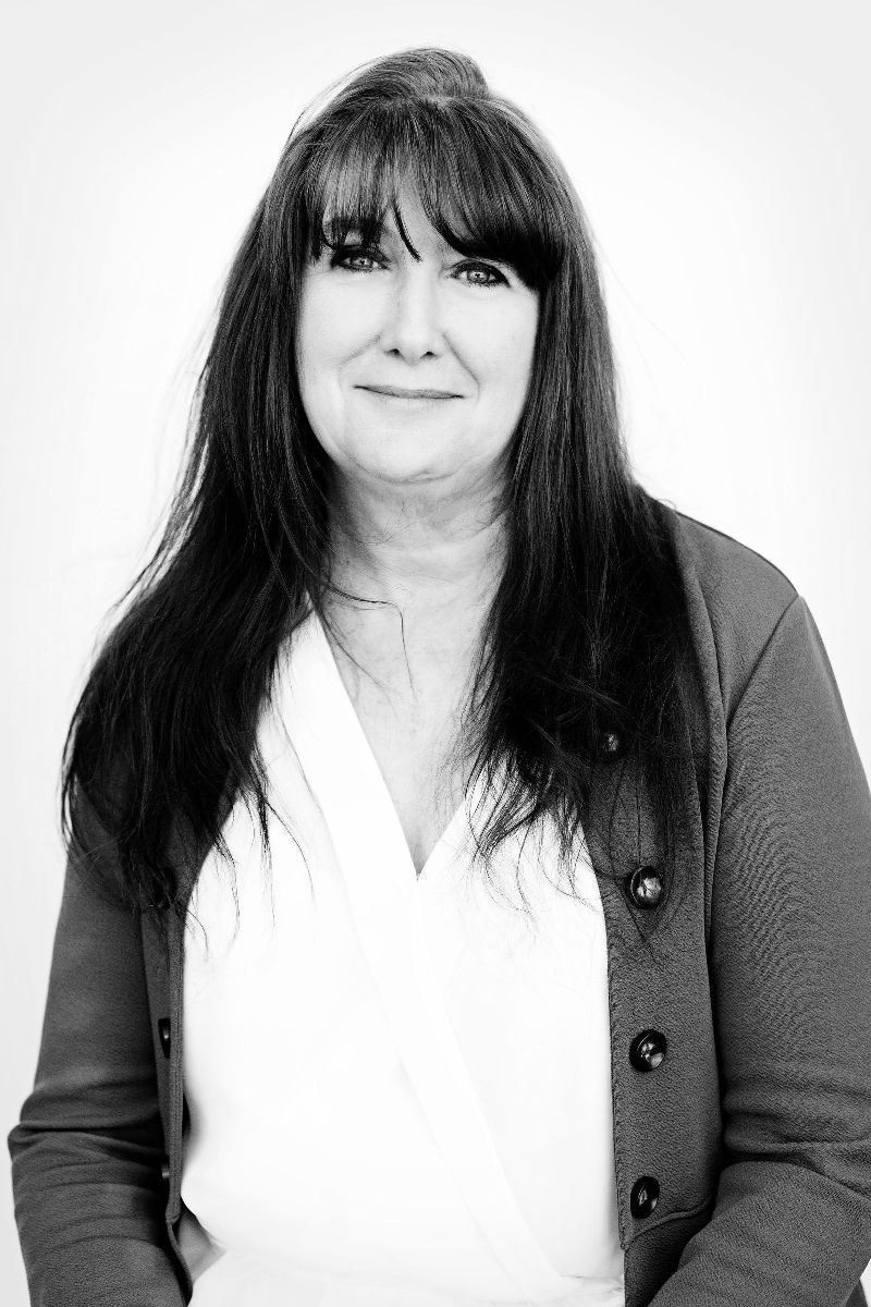 Woman with dark hair and bangs wearing a white shirt and gray cardigan, smiling.