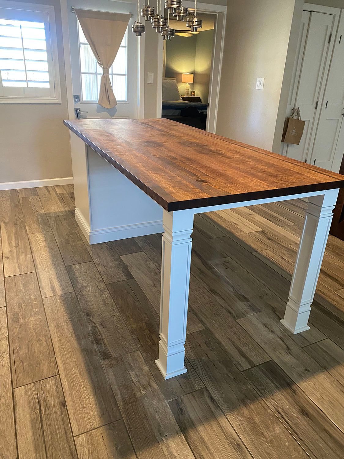 A wooden table with white legs is sitting on a wooden floor in a kitchen.