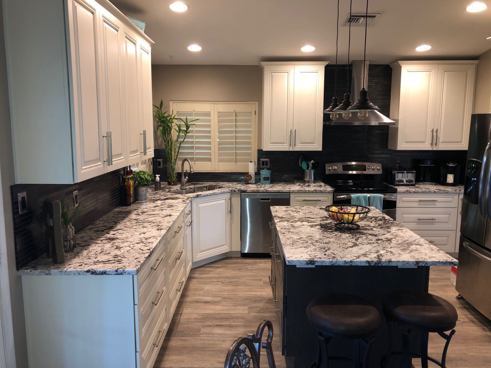 A kitchen with white cabinets , granite counter tops , stainless steel appliances and a large island.