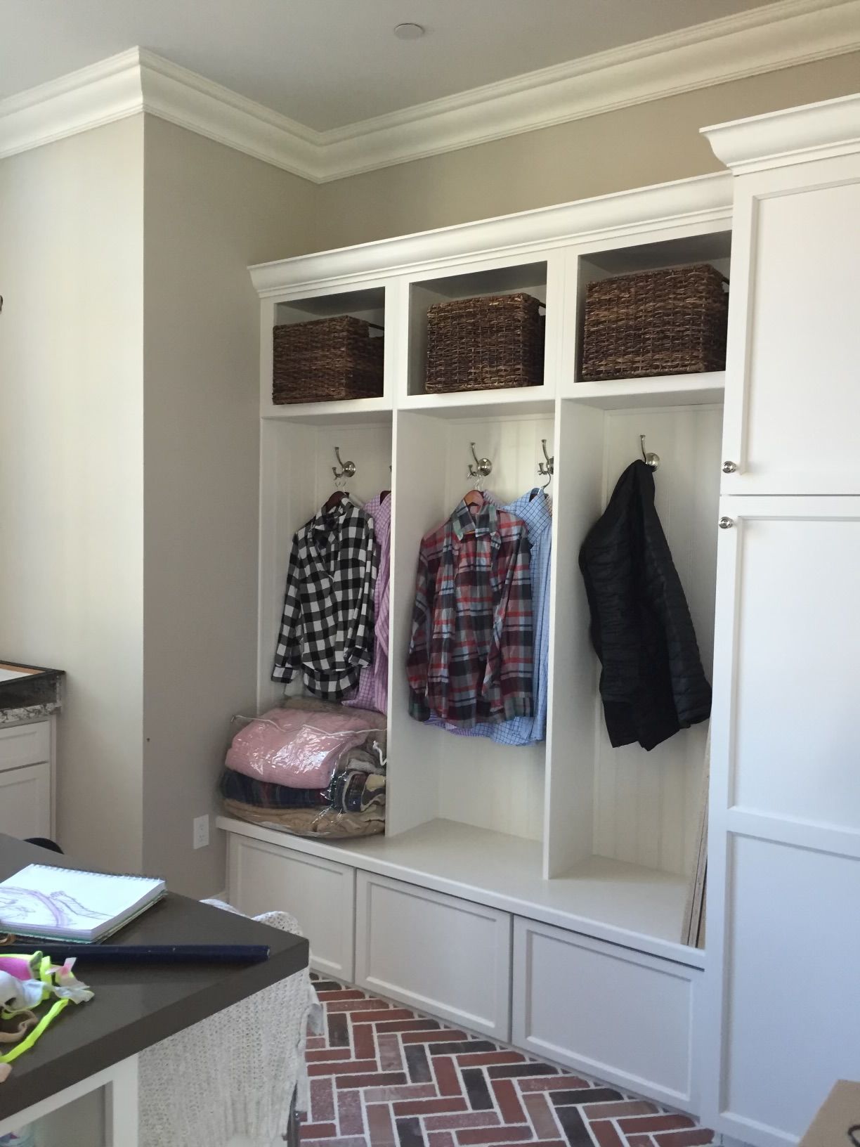 A laundry room with white cabinets and clothes hanging on hooks