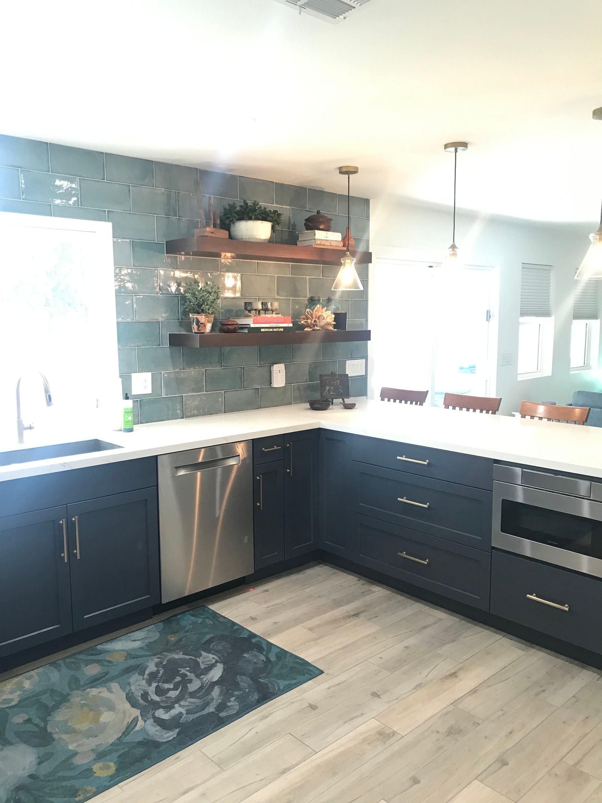 A kitchen with blue cabinets , stainless steel appliances , a rug and a window.