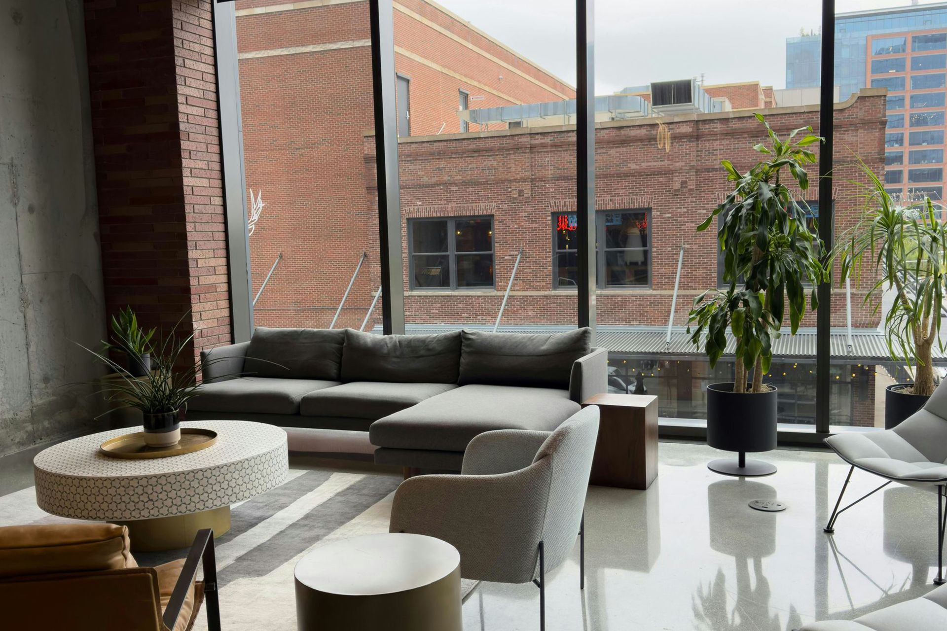 Modern lounge with gray sofas, round tables, and large windows overlooking brick buildings