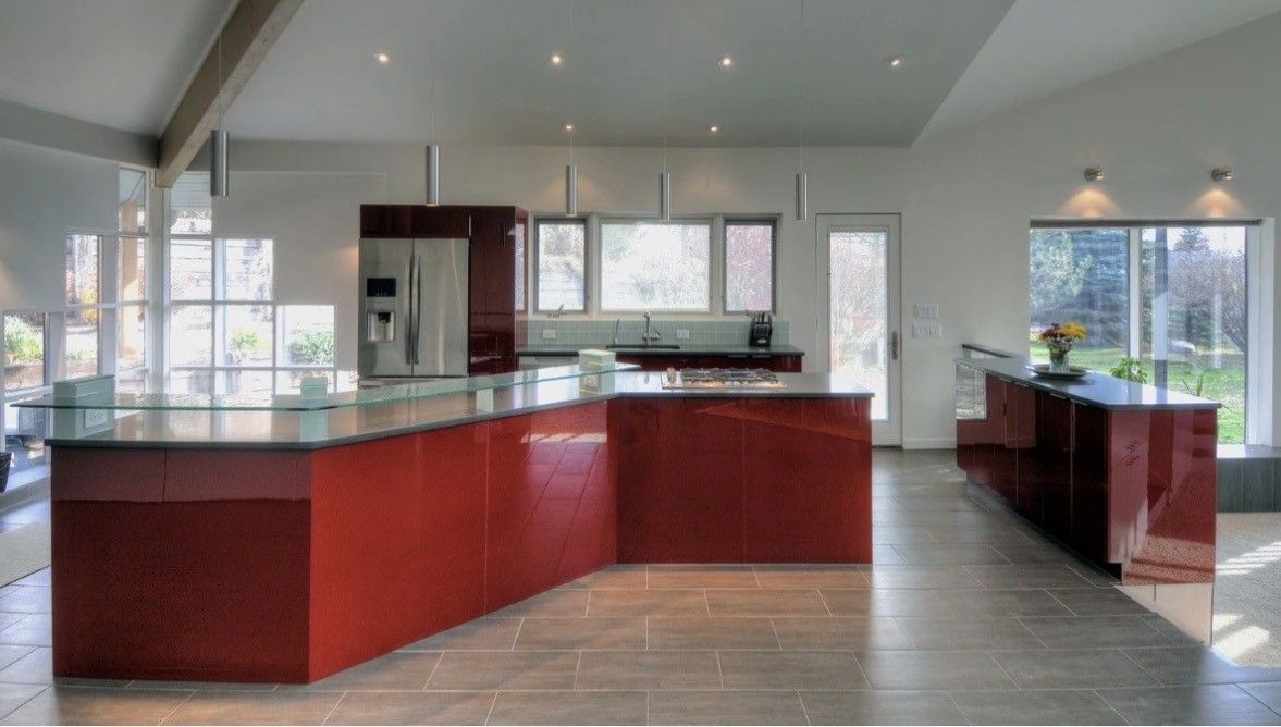 Modern empty kitchen with red cabinets, dark countertops, and large windows