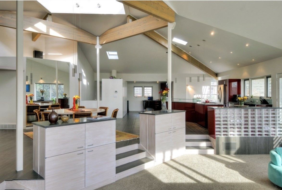 Modern open-plan kitchen and living room with high vaulted ceiling, white cabinets, and sunlit windows