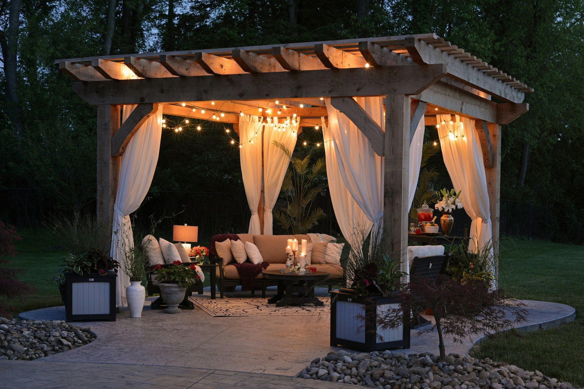 Outdoor cabana with sheer curtains and warm string lights, furnished for a cozy evening lounge.