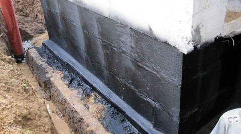 Exterior wall corner with black waterproofing coating along the foundation near the ground