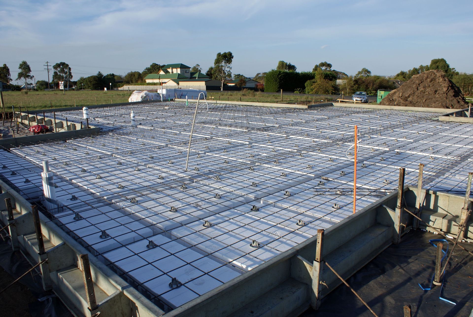 Construction site with a large concrete foundation slab covered in rebar under a clear sky