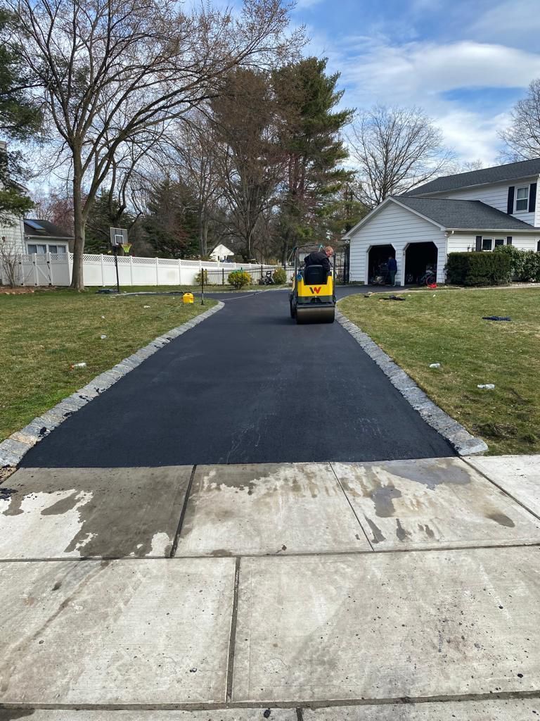 Freshly paved driveway with a small yellow utility vehicle near a white house and garage