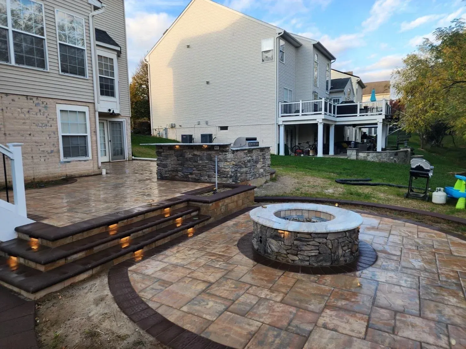 Stone patio with circular fire pit, tiered steps, and apartment buildings in a landscaped courtyard