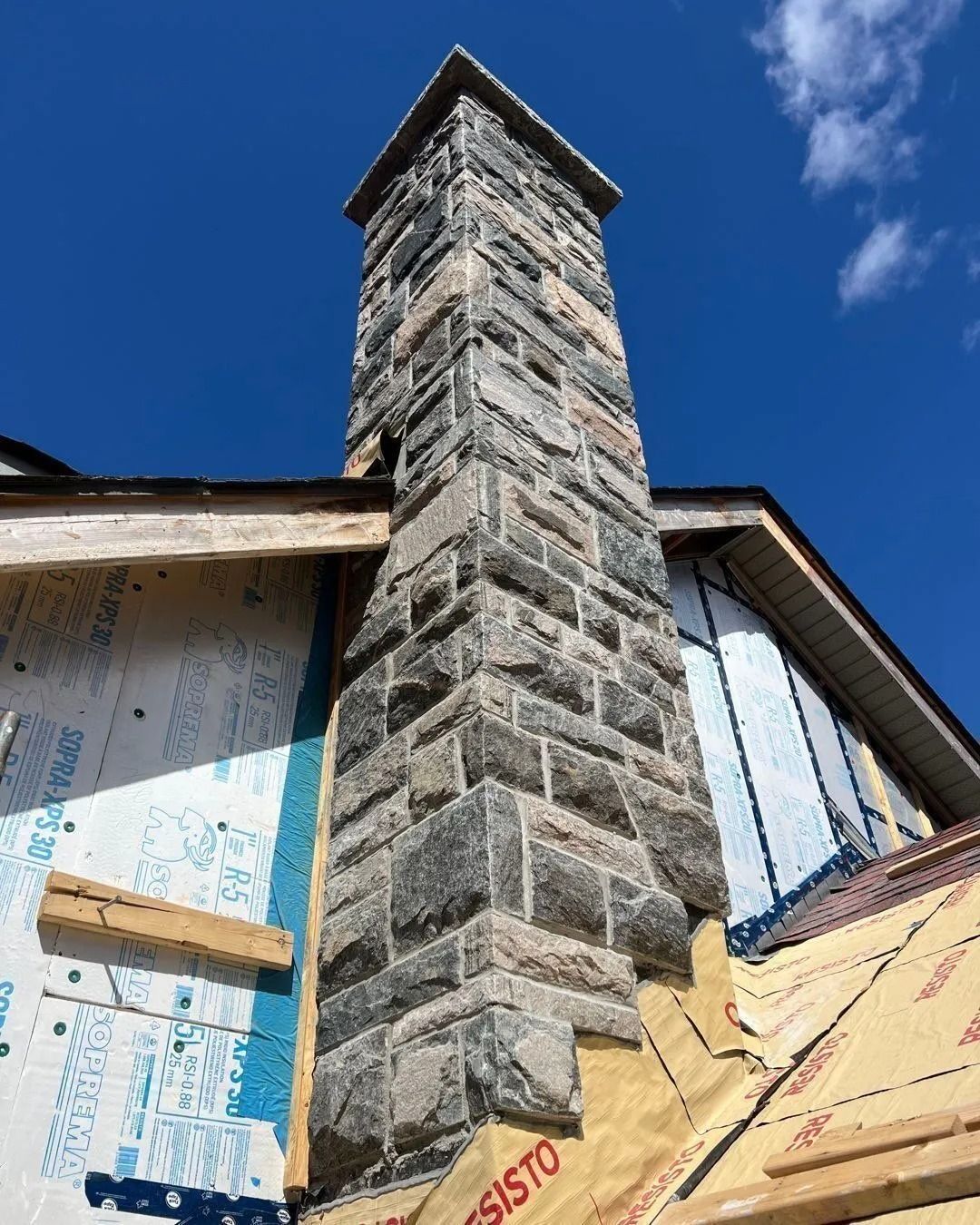 Stone chimney on a house under construction against a blue sky.