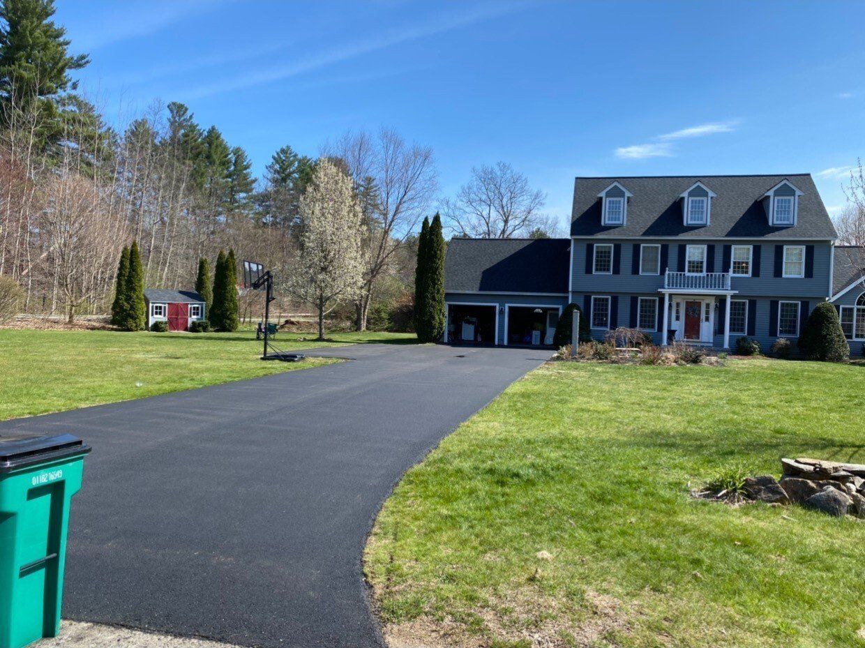 Suburban house with paved driveway, green lawn, and blue trash bin under a clear sky