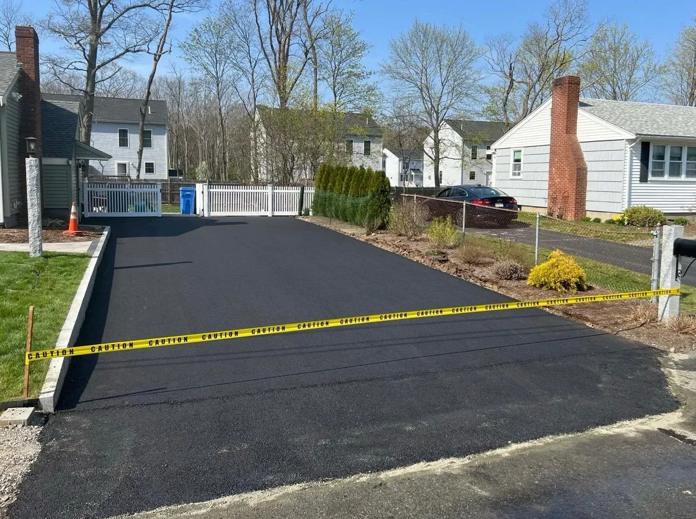 Freshly paved black driveway with yellow caution tape in a suburban yard