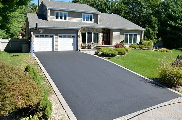 Suburban house with a long black driveway, white garage doors, and a green front lawn.