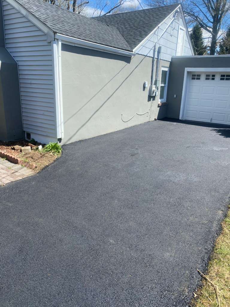 Freshly paved driveway beside a light-colored house and garage on a sunny day