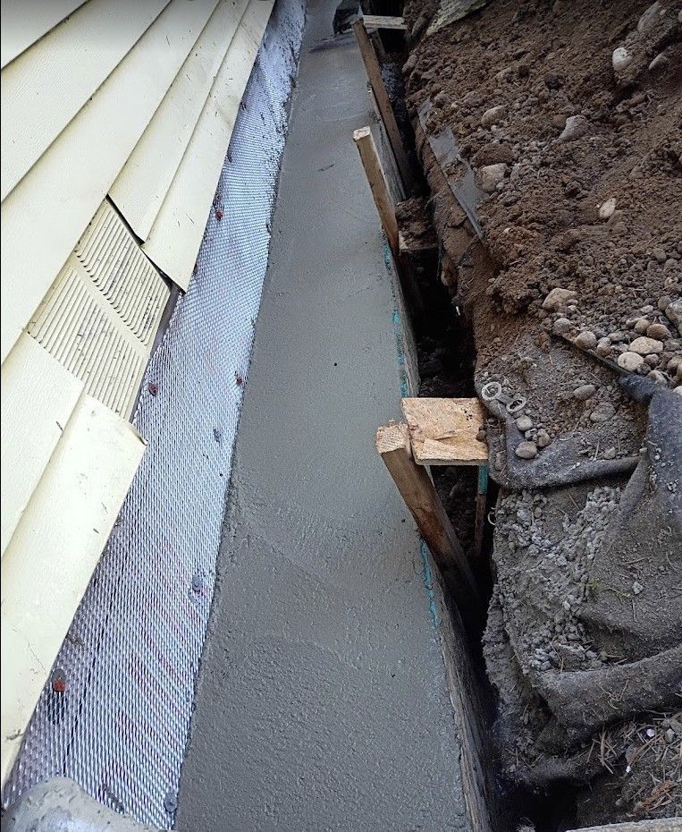 Fresh concrete walkway beside a house foundation and exposed soil trench