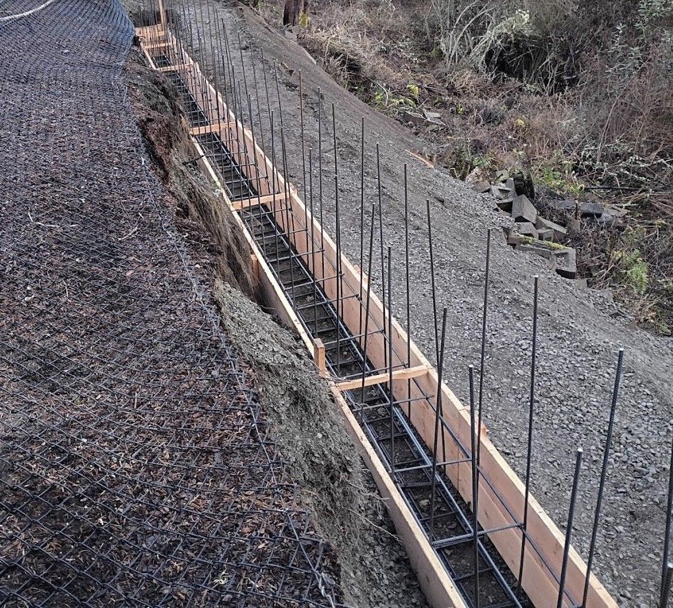 Concrete foundation trench with rebar and wooden forms along a gravel slope
