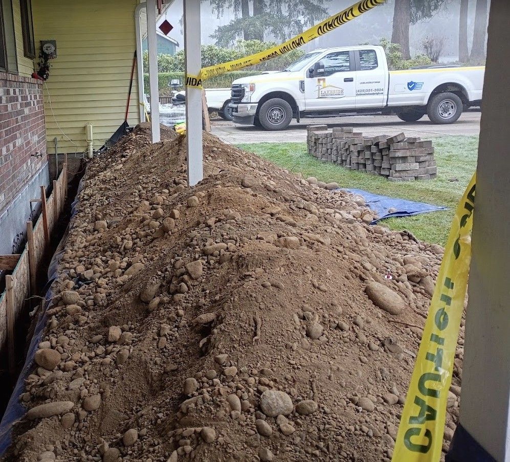 Large dirt pile beside a house under construction, with caution tape and a white utility truck in the background