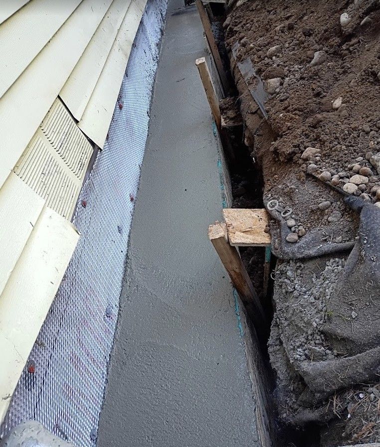 Fresh concrete trench beside house foundation with exposed dirt and wooden supports