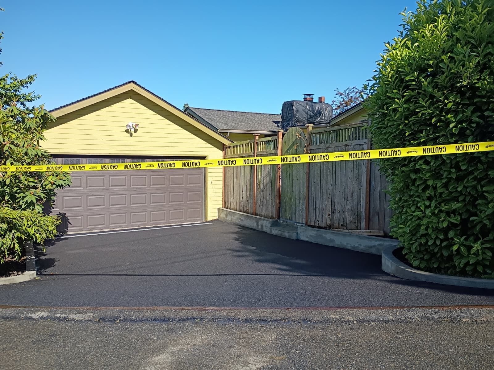 Yellow house with garage blocked by caution tape across driveway and fence under blue sky