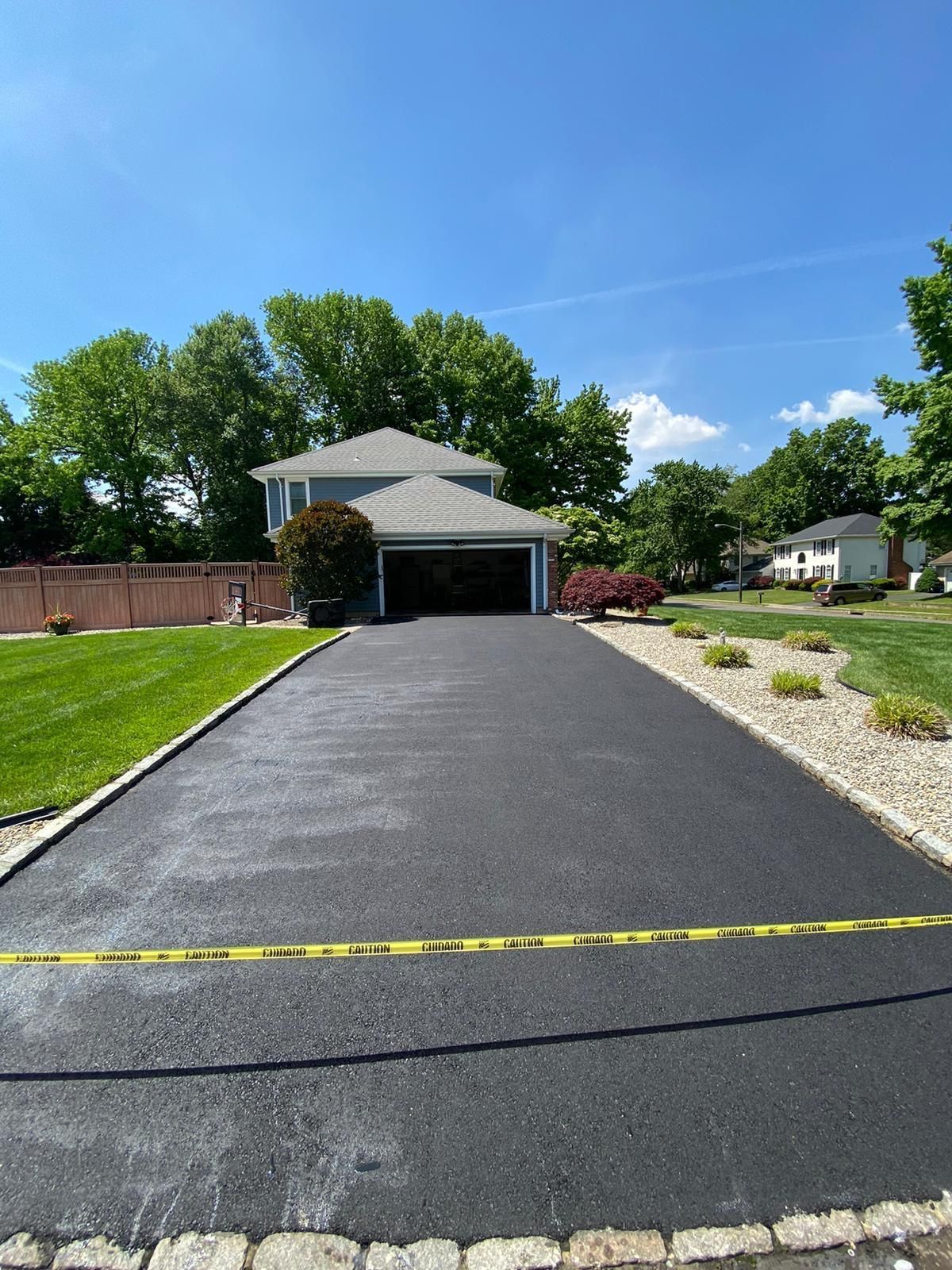Long black driveway leading to a detached garage under a blue sky, with lawn and trees on both sides.
