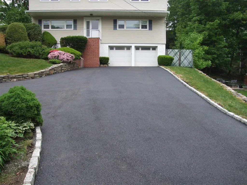 Freshly paved driveway leading to a white two-car garage and house with landscaped front yard