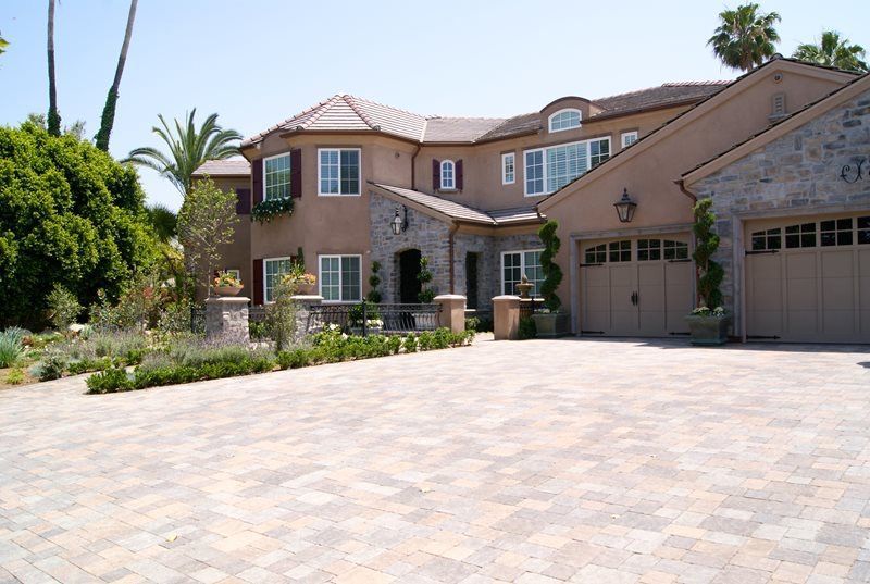 Large beige suburban house with a three-car garage and a wide paved driveway in bright daylight