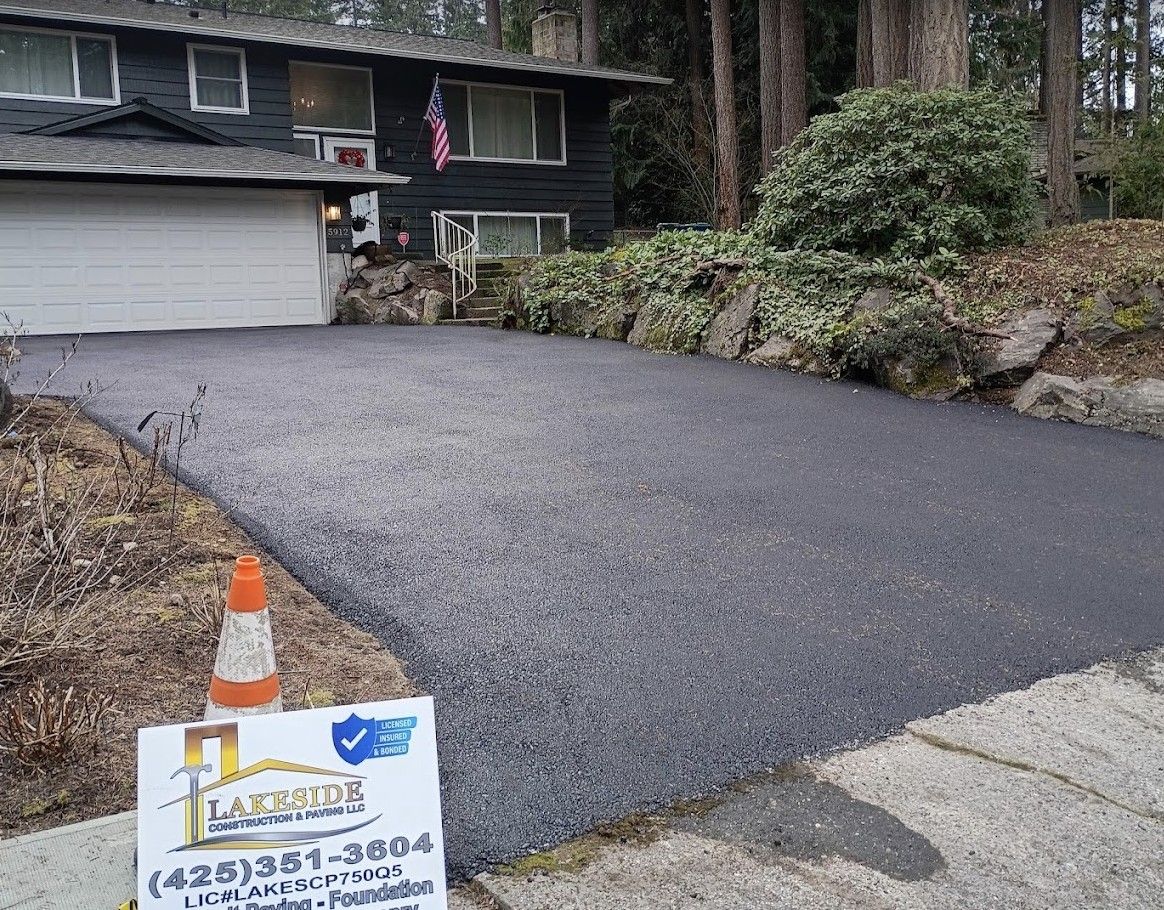 Freshly paved driveway beside a house with a garage, rock landscaping, and a small sign in the foreground.