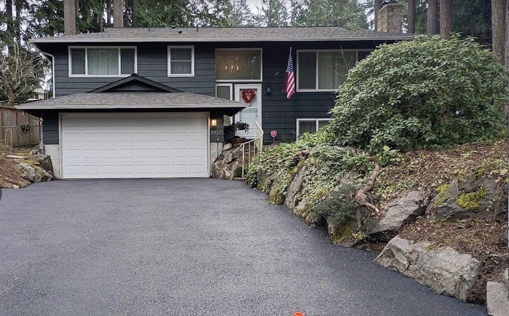 Suburban house with gray siding, two-car garage, gravel driveway, and an American flag by the front door