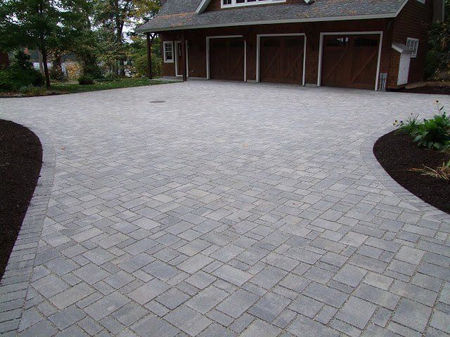 Paved driveway leading to a brick garage with three doors and landscaped edges