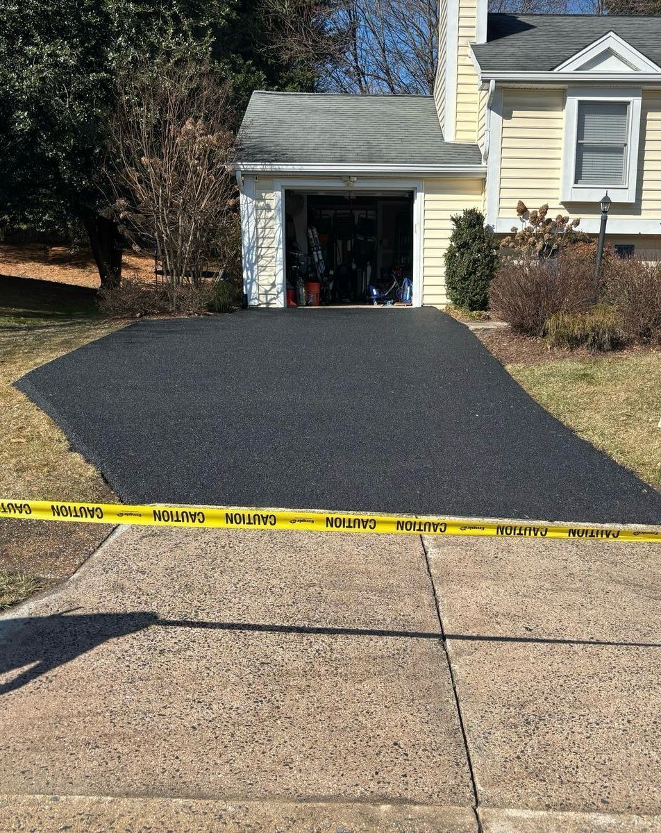 Fresh black asphalt driveway leading to a house garage, with yellow caution tape across the front.